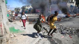 Seorang wanita dengan putrinya berjalan melewati barikade yang dipasang oleh anggota polisi saat demonstrasi pecah di Port-au-Prince, (AP PHOTO/ODELYN JOSEPH)